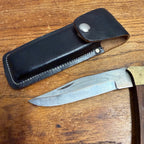 Vintage Stainless Steel Folding Knife With Brass-Accented Wooden Handle and Black Leather Sheath