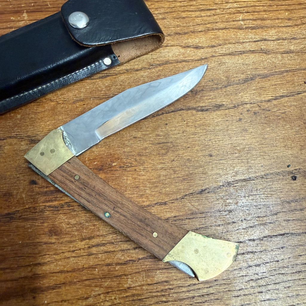 Vintage Stainless Steel Folding Knife With Brass-Accented Wooden Handle and Black Leather Sheath