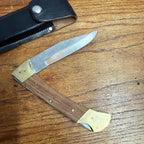 Vintage Stainless Steel Folding Knife With Brass-Accented Wooden Handle and Black Leather Sheath
